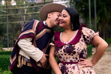 Şilili huasolar gibi giyinmiş, romantik poz veren ve geleneksel bir Şili dansı olan Cueca 'yı öpüp dans eden genç bir çiftin portresi. Şili gelenekleri, kutlamalar ve kültür.                          