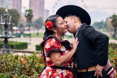 Şilili huasolar gibi giyinmiş, romantik poz veren ve geleneksel bir Şili dansı olan Cueca 'yı öpüp dans eden genç bir çiftin portresi. Şili gelenekleri, kutlamalar ve kültür.    