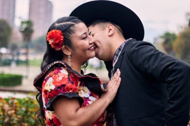 Şilili huasolar gibi giyinmiş, romantik poz veren ve geleneksel bir Şili dansı olan Cueca 'yı öpüp dans eden genç bir çiftin portresi. Şili gelenekleri, kutlamalar ve kültür.    