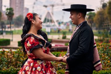 Şilili genç bir Latin çift, Şilili huasolar gibi giyinmiş, çok romantik ve neşeli, el ele tutuşuyorlar, geleneksel bir Şili dansı olan cueca 'yı öpüp dans etmek üzereler. Şili Bağımsızlık Günü kutlamaları.