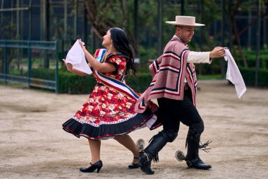 Şilili huasolar gibi giyinmiş, açık havada neşeyle dans eden genç bir çiftin portresi. Geleneksel Şili dansı. Şili gelenekleri, kutlamalar.
