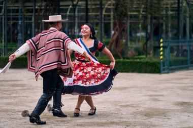 Şilili huasolar gibi giyinmiş, açık havada neşeyle dans eden genç bir çiftin portresi. Geleneksel Şili dansı. Şili gelenekleri, kutlamalar.