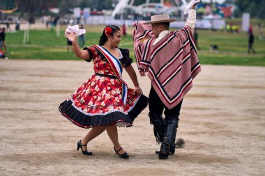 Şilili huasolar gibi giyinmiş, açık havada neşeyle dans eden genç bir çiftin portresi. Geleneksel Şili dansı. Şili gelenekleri, kutlamalar.