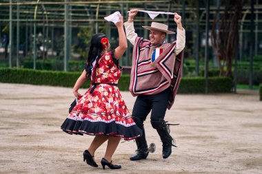 Şilili huasolar gibi giyinmiş, açık havada neşeyle dans eden genç bir çiftin portresi. Geleneksel Şili dansı. Şili gelenekleri, kutlamalar.