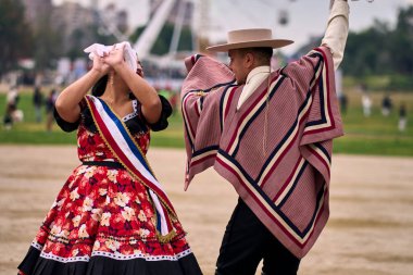 Şilili huasolar gibi giyinmiş, açık havada neşeyle dans eden genç bir çiftin portresi. Geleneksel Şili dansı. Şili gelenekleri, kutlamalar.