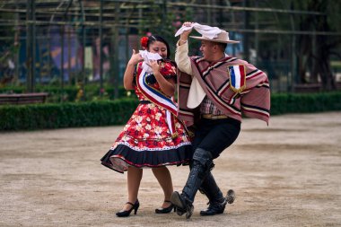 Şilili huasolar gibi giyinmiş, açık havada neşeyle dans eden genç bir çiftin portresi. Geleneksel Şili dansı. Şili gelenekleri, kutlamalar.