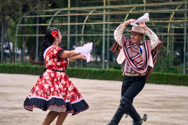Şilili huasolar gibi giyinmiş, açık havada neşeyle dans eden genç bir çiftin portresi. Geleneksel Şili dansı. Şili gelenekleri, kutlamalar.