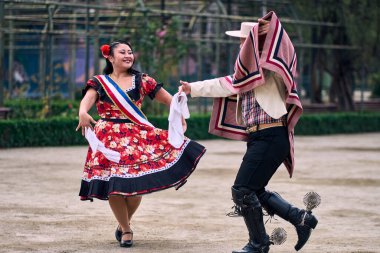 Şilili huasolar gibi giyinmiş, açık havada neşeyle dans eden genç bir çiftin portresi. Geleneksel Şili dansı. Şili gelenekleri, kutlamalar.