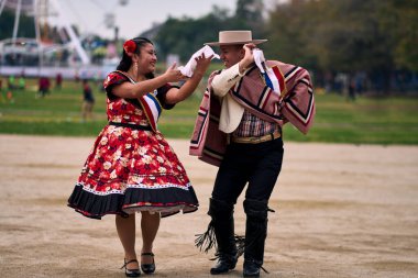 Şilili huasolar gibi giyinmiş, açık havada neşeyle dans eden genç bir çiftin portresi. Geleneksel Şili dansı. Şili gelenekleri, kutlamalar.