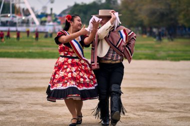 Şilili huasolar gibi giyinmiş, açık havada neşeyle dans eden genç bir çiftin portresi. Geleneksel Şili dansı. Şili gelenekleri, kutlamalar.