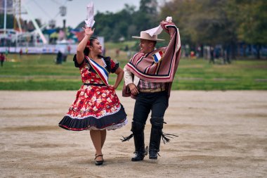 Şilili huasolar gibi giyinmiş, açık havada neşeyle dans eden genç bir çiftin portresi. Geleneksel Şili dansı. Şili gelenekleri, kutlamalar.