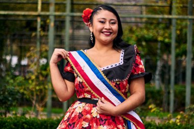 Şili huasası gibi giyinmiş, neşeli bir şekilde gülümseyen ve geleneksel Şili dansı olan cueca dansı için poz veren güzel bir genç kadının portresi. Şili gelenekleri.