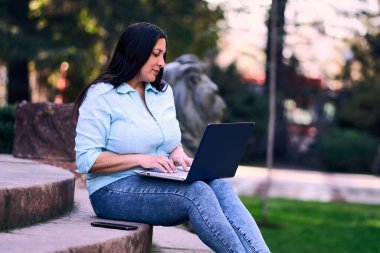 Evde dizüstü bilgisayarıyla çalışan, gülümseyen ve aynı zamanda cep telefonunu kullanan güzel, olgun bir Latin kadın. İş kadını, pazarlama, ev ofisi..                               