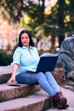 Evde dizüstü bilgisayarıyla çalışan, gülümseyen ve aynı zamanda cep telefonunu kullanan güzel, olgun bir Latin kadın. İş kadını, pazarlama, ev ofisi..                               