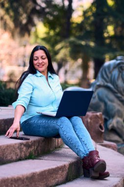 Evde dizüstü bilgisayarıyla çalışan, gülümseyen ve aynı zamanda cep telefonunu kullanan güzel, olgun bir Latin kadın. İş kadını, pazarlama, ev ofisi..                               