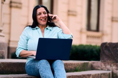Arka bahçesinde bilgisayarının başında mutlu bir şekilde gülümseyen ve aynı zamanda cep telefonuna cevap veren güzel, olgun bir Latin. İş kadını, pazarlama, ev ofisi..                