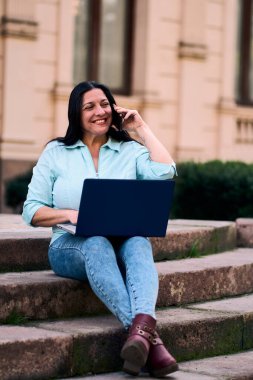 Arka bahçesinde bilgisayarının başında mutlu bir şekilde gülümseyen ve aynı zamanda cep telefonuna cevap veren güzel, olgun bir Latin. İş kadını, pazarlama, ev ofisi..                