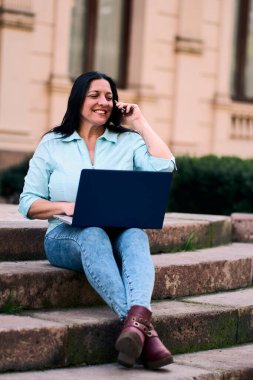 Arka bahçesinde bilgisayarının başında mutlu bir şekilde gülümseyen ve aynı zamanda cep telefonuna cevap veren güzel, olgun bir Latin. İş kadını, pazarlama, ev ofisi..                