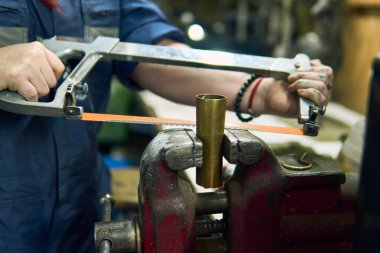 View of a Latina woman's hands working in a mechanical workshop, using machines and tools, bending metal, polishing, and cleaning. Wearing a blue suit, she does metal crafts. Independent, artisan.                               