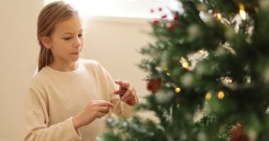 Çocuk Noel ağacına orman konisi asıyor. Güzel küçük kız, Noel ağacını orman konisiyle süslüyor. Mutlu aile, çocukluk, Noel. Noel arifesinde oynayan bir çocuk. Tatil kutlaması. Yüksek