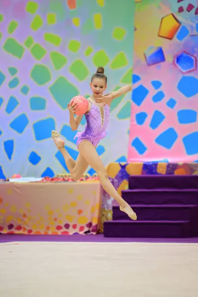 stock image Young gymnast executing a stunning leap while holding a ball. Vivid background enhances her elegance.