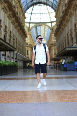 Genç bir adam, parlak ve canlı mimari ile süslenmiş çarpıcı tarihi bir oyun salonunda fotoğraf için güven içinde poz veriyor.