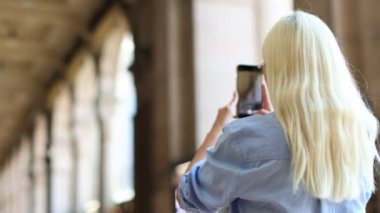 Güzel, uzun sarı saçlı genç bir kadın çarpıcı bir mimari alanda büyüleyici fotoğraflar yakalıyor.