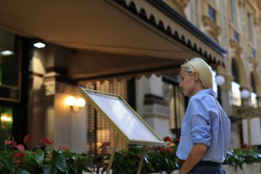 Şık bir kadın, şık bir kafe dışında lüks bitkilerle süslenmiş geniş bir menüyü inceliyor.