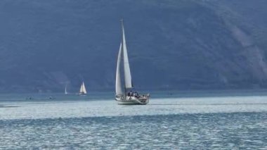 Bir yelkenli zarif bir şekilde gölün sakin ve sakin sularında süzülür. Uzaktaki sakin dağlar tarafından çerçevelenir.
