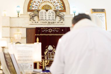 Bir sinagogda kendini adamış bir kişi Tevrat ve kutsal unsurlara odaklanmış bir şekilde duruyor.