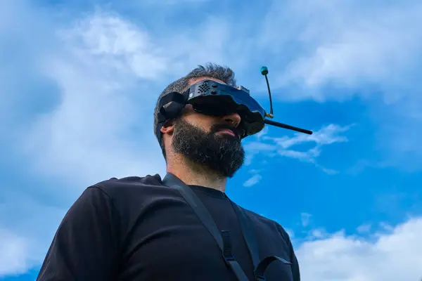 Kendinden emin FPV insansız hava aracı pilotu uçan aracı açık havada mavi gökyüzünde uçuruyor. Drone askeri okul eğitmeni.