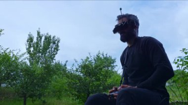 FPV insansız hava aracı pilotu helikopter kumandası tutuyor, kulaklığı çıkarıyor. Kafkas erkek helikopter vr operatörü uçak okulunda çokgen alanında uçmayı öğreniyor.