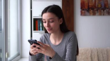 Güzel bir kadın akıllı telefonda konuşurken mutlu bir şekilde gülümsüyor güzel bir genç kadın evde akıllı telefonuyla sohbet ederken mutlulukla gülümsüyor. Parlak ve neşeli bir atmosfer, kavramlar için mükemmel.