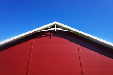 Klasik bir binanın kırmızı cephesini ve beyaz kirişlerini yakalayan minimalist bir mimari çekim, açık mavi gökyüzüne karşı ayarlanmış. Bu resim zamansız tasarımın zarafetini vurgular