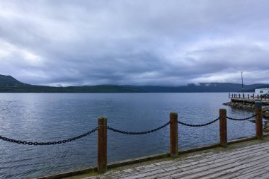 Sakin bir körfez ya da göle bakan tahta bir iskeleden huzurlu bir manzara. Ufuk çizgisinde uzak dağlar var. Doğa sahneleri, rahatlama ve manzaralı güzellik için ideal.