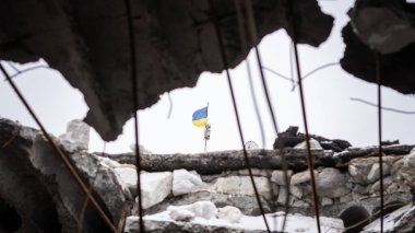 Kherson bölgesinin işgalsiz köyündeki yıkık okulun tavanındaki delikten görünen Ukrayna bayrağı. Ukrayna 'daki savaşın gerçekleri