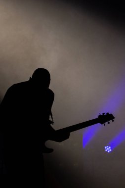 Sahnede, konser sırasında duman makinesinden çıkan bir gitaristin silueti.