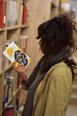 Kitapçıda okumak için kitap seçen genç bir kadın ciddi ve meraklı.