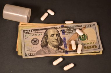 100 dolarlık banknotlar ve siyah arka planda farklı türde haplar.