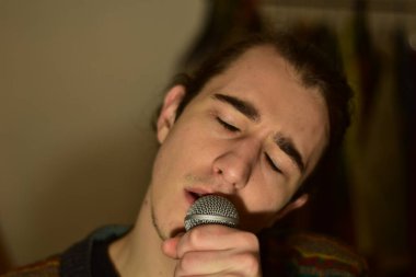 White Caucasian male singing on a microphone at home passionately 