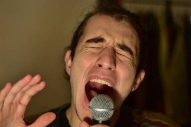 White Caucasian male singing on a microphone at home passionately 