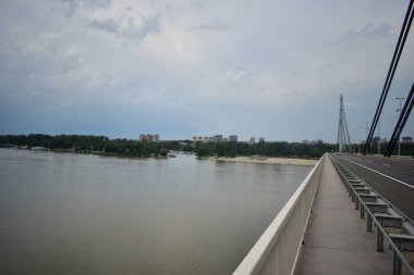 Novi Sad şehri ve Tuna Nehri üzerindeki köprü. Sahilde insanlar var..