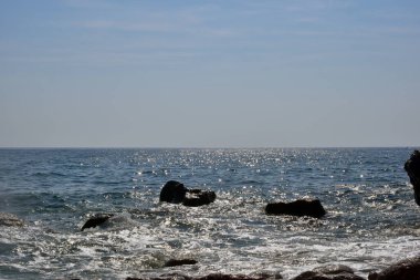 Kayalık sahilde deniz dalgası sıçradı. Okyanus dalgaları kayalara çarpıyor. Güneşli bir gün doğa arka plan fotoğrafçılığı.