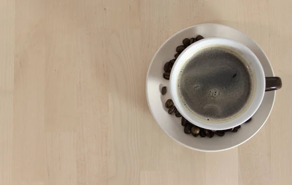Tabağında kahve çekirdekleri olan bir fincan kahvenin ahşap bir masanın üzerindeki görüntüsü. Kafeteryada. Kahvaltı..