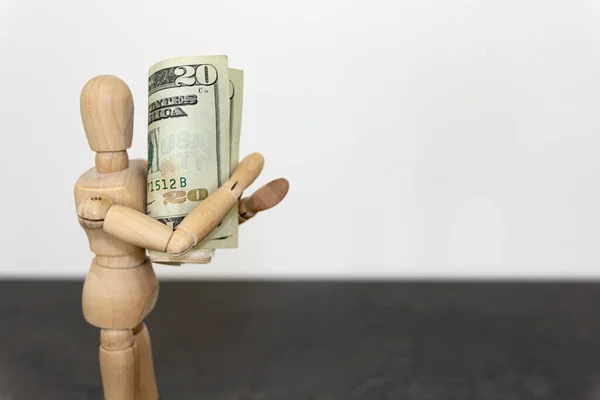 Siyah bir masanın üzerinde beyaz bir arka planda 20 dolarlık banknot tutan bir mankenin yakın plan çekimi. Görüntü finansal başarı ve refahı temsil ediyor..