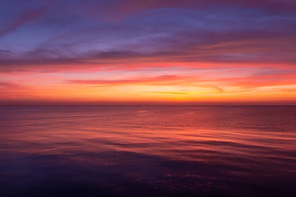 stock image Colorful sunrise with oranges, purples, and blues illuminating the sky and sea.