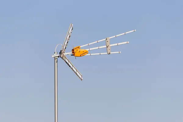 Uzun bir anten açık mavi bir gökyüzüne karşı duruyor, birden fazla kol dışa doğru uzanıyor..