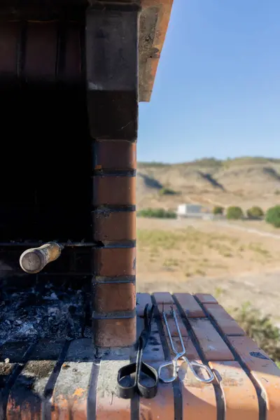 Yanı başında bir çift maşayla açık mavi gökyüzünün altında duran bir ızgara..