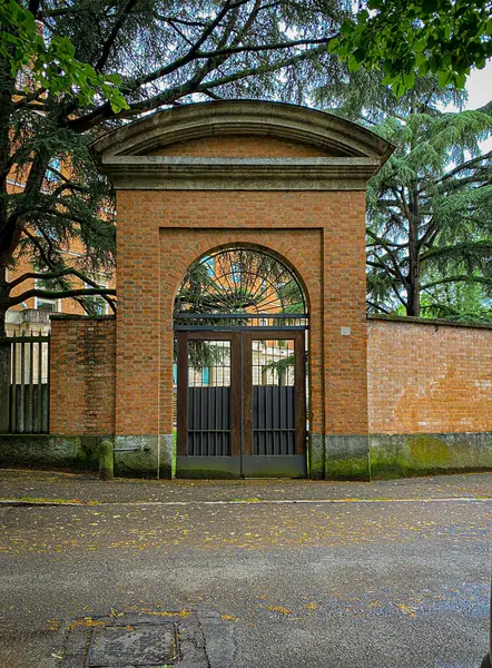 Siyah kapılı tuğla bir kemer, klasik mimari ve modern tasarım elementlerinin bir karışımını sergileyen bir binanın önünde duruyor.