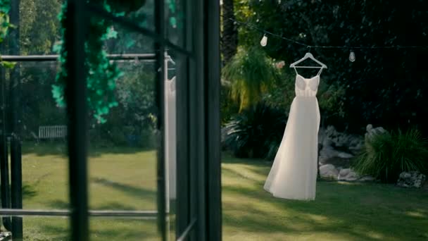 ガーランドの庭にウェディングドレスが掛かります ドレスは風の中で動き 窓に映し出される 結婚式のための完璧な日に緑の庭での写真 似ている — ストック動画